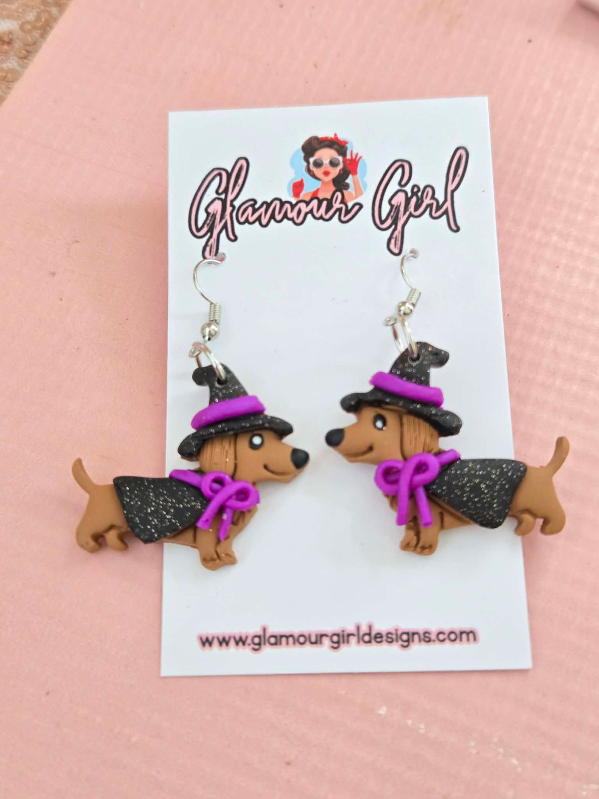 Original photo of purple witch dachshund earrings with black hats, capes, purple bows and silver hooks on a Glamour Girl display card.